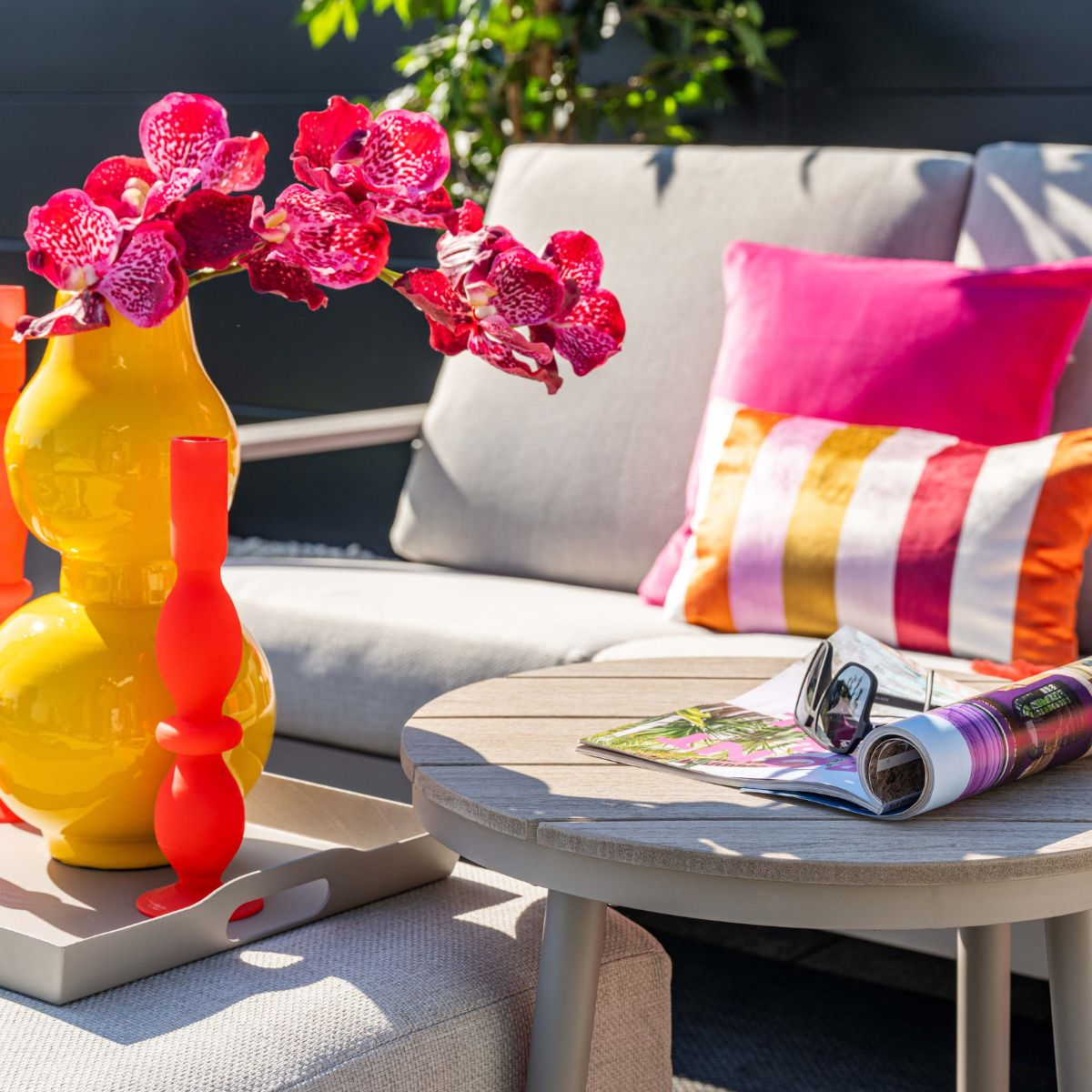 Yellow vase with red orchids, red vases on tray next to sofa with colorful pillows.