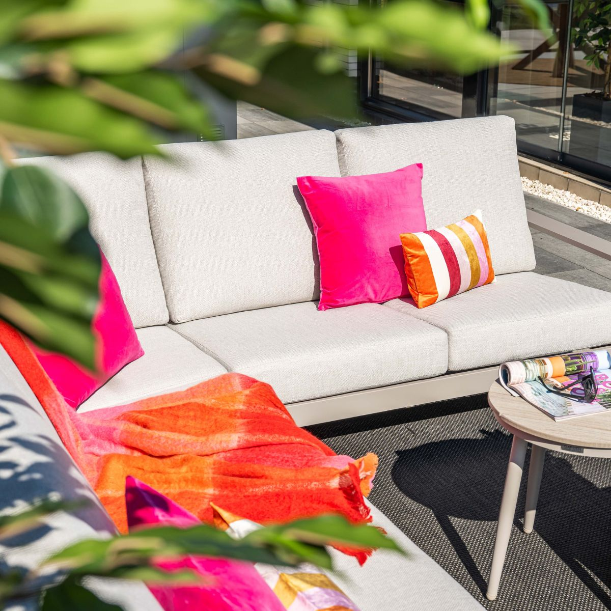 A cream sofa with colorful cushions and a throw, magazines on a side table.