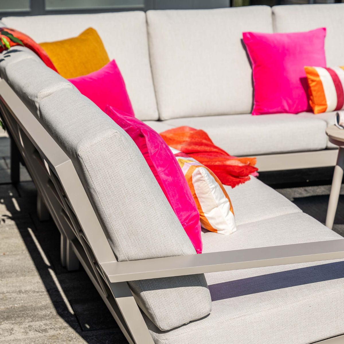 A light gray outdoor sofa with colorful pillows and a throw blanket.