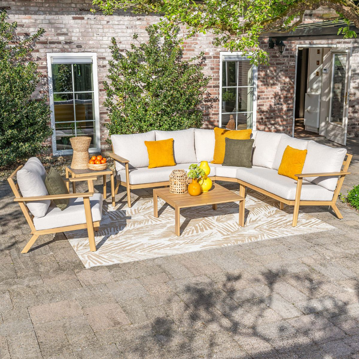 A modern outdoor sectional sofa with light cushions in front of a brick wall.