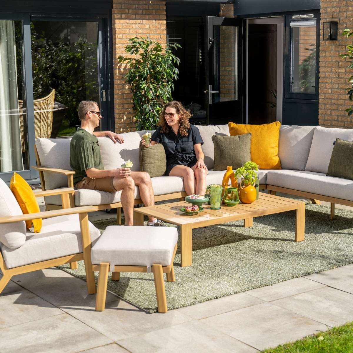 A couple relaxes on a patio sofa with drinks and snacks.