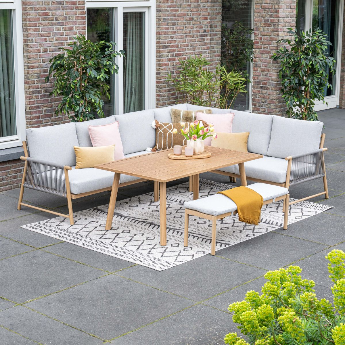 Een moderne buiten zithoek met hoekbank, salontafel en bankje op een terras.