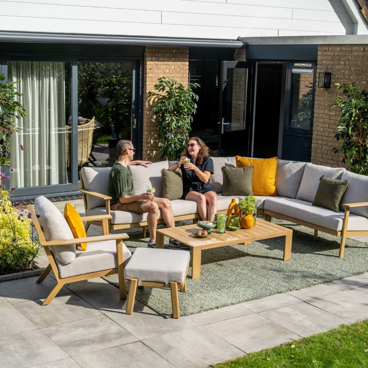 A couple sits on an outdoor sectional sofa, enjoying drinks in a garden.