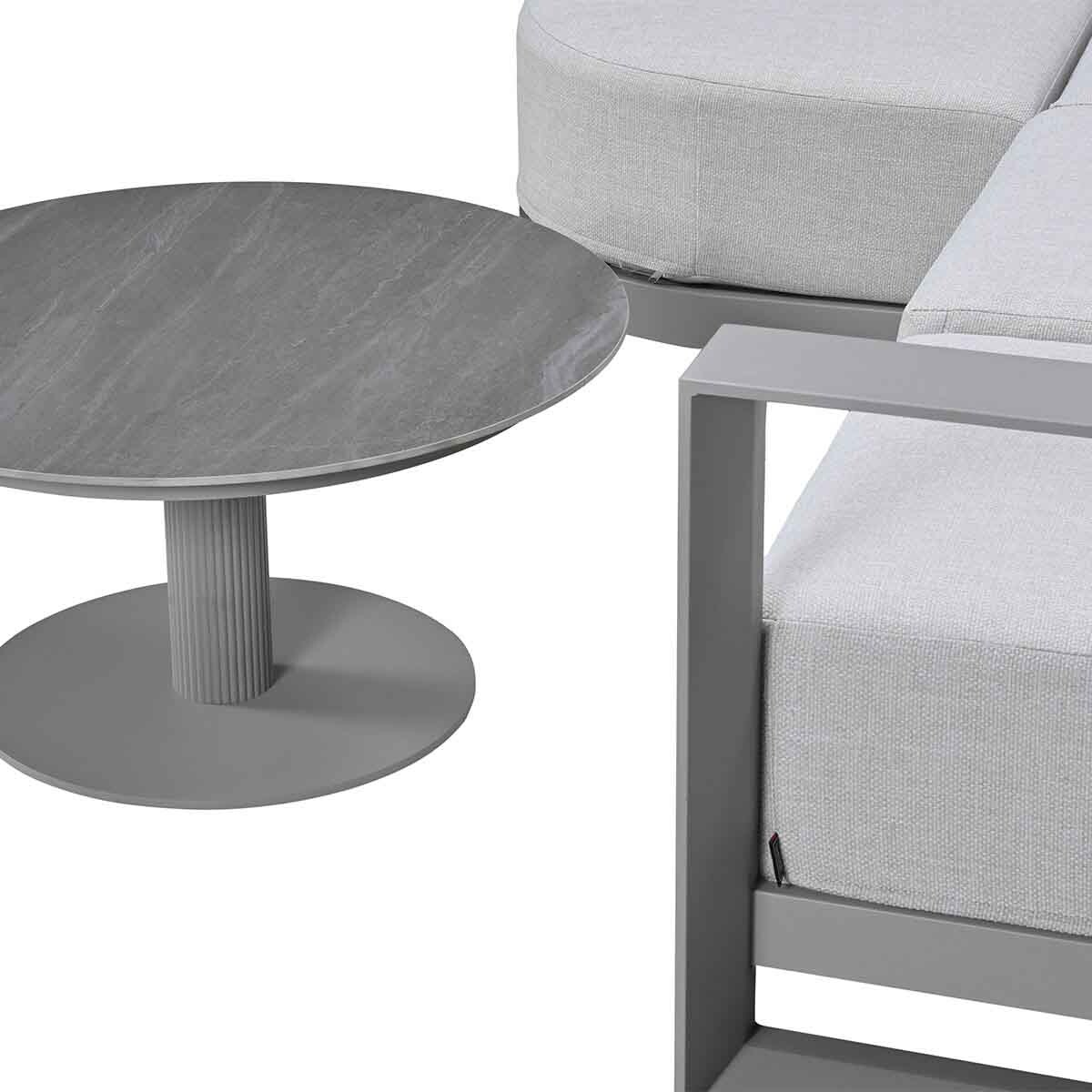 Gray round table next to a gray sofa with light gray cushions.