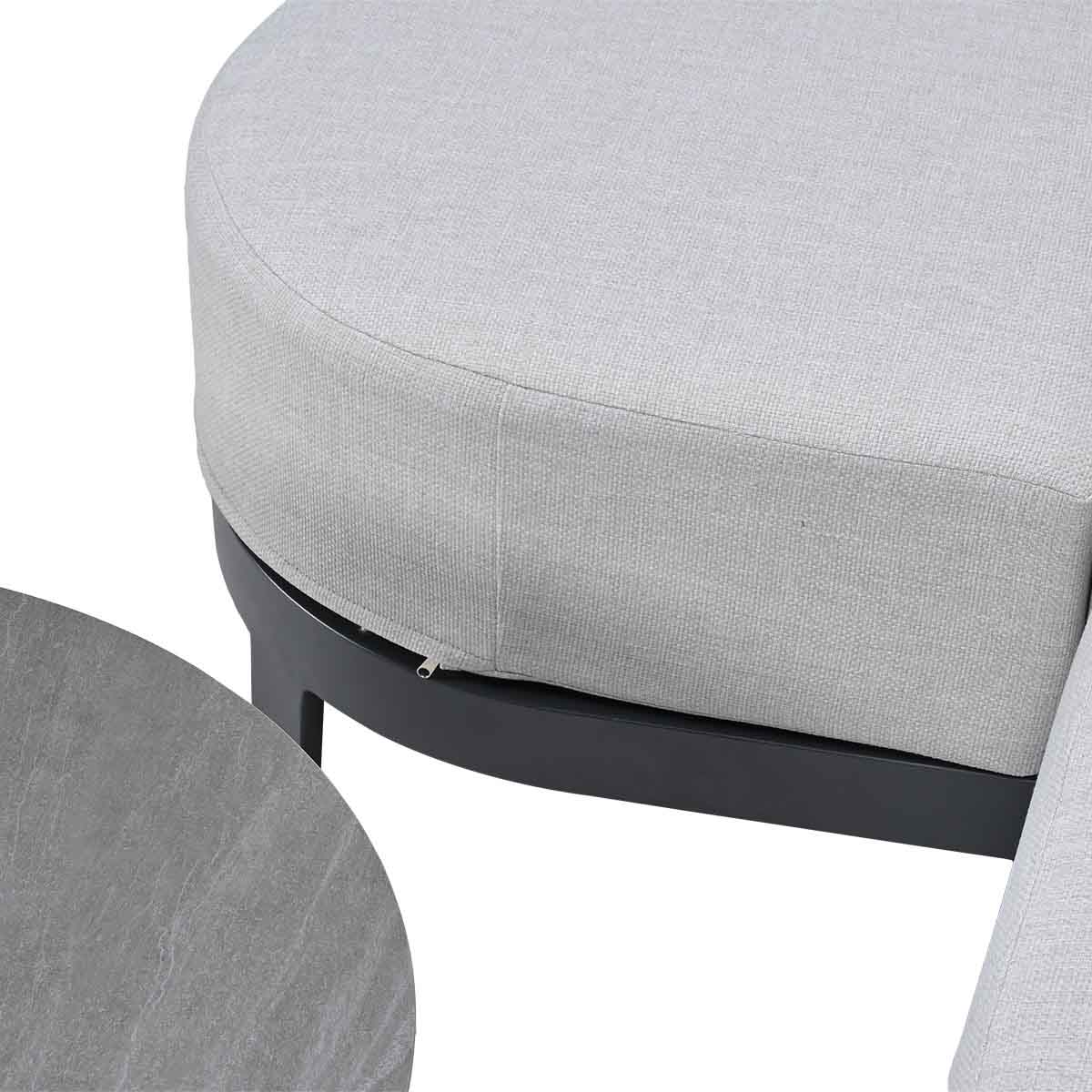 A grey upholstered outdoor sofa next to a round stone table.