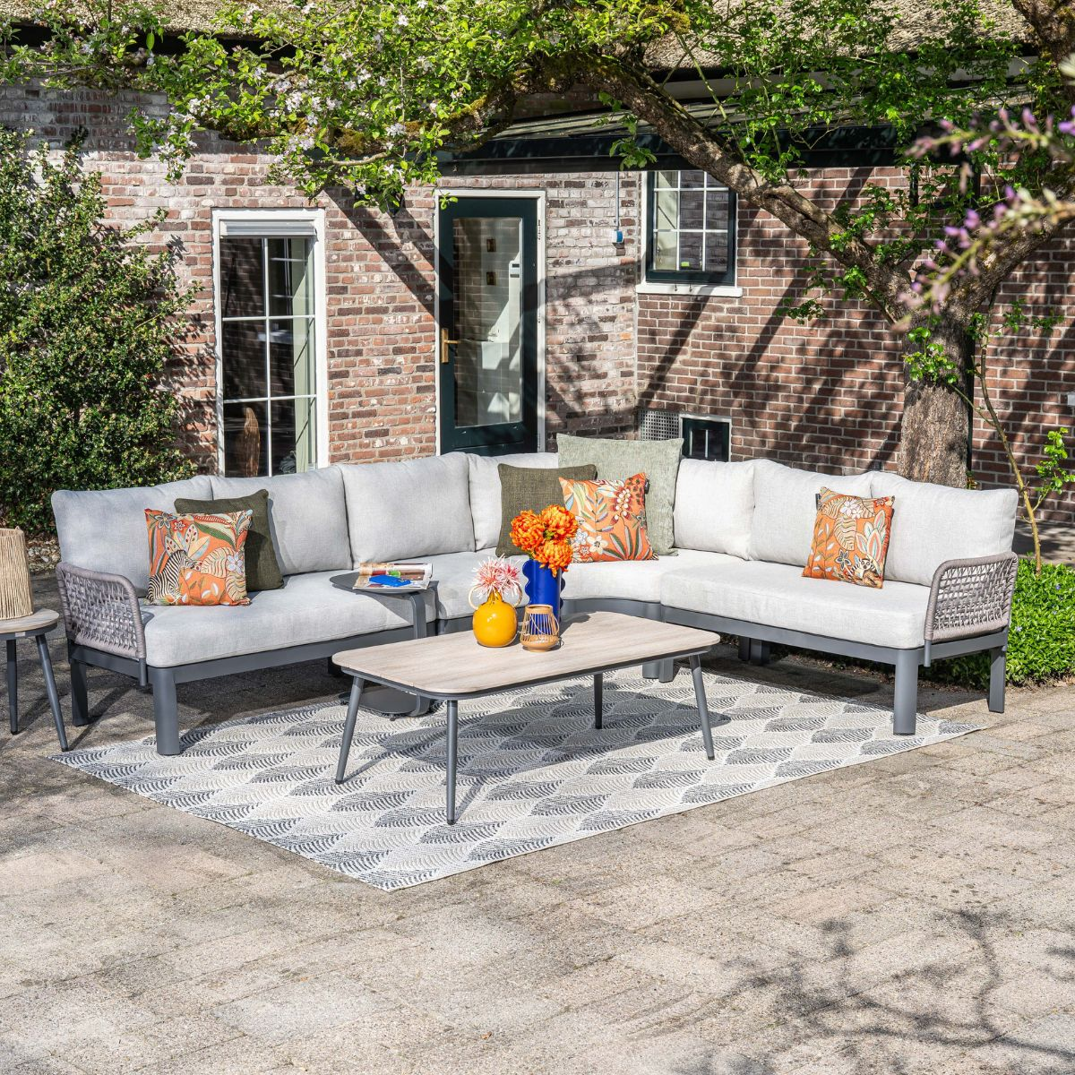 Outdoor sectional sofa with coffee table on a patio, with a brick house in the background.