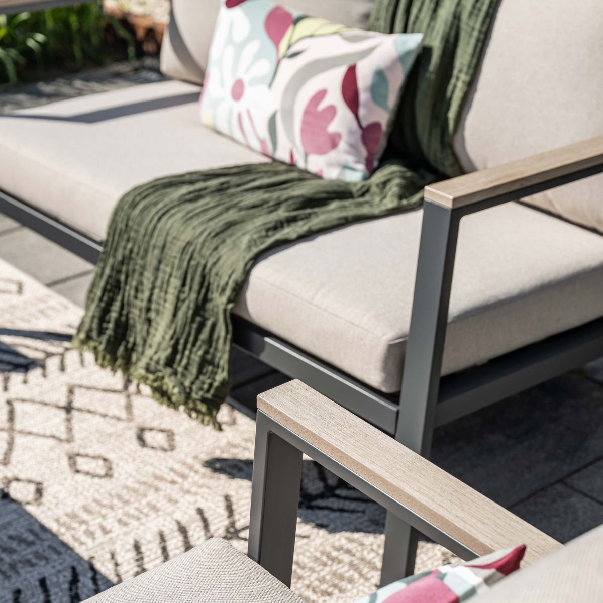 Outdoor furniture with a cushion and blanket on a rug.