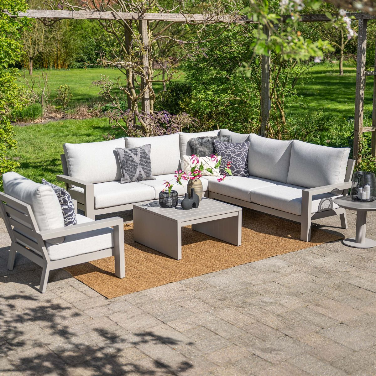 Gray outdoor sofa and chair set with coffee table on patio, green garden.