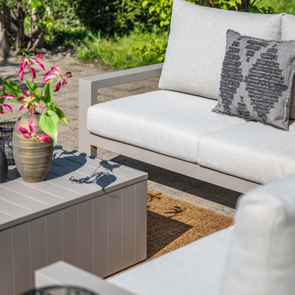Gray outdoor sofa with white cushions and a vase of pink flowers on a table.