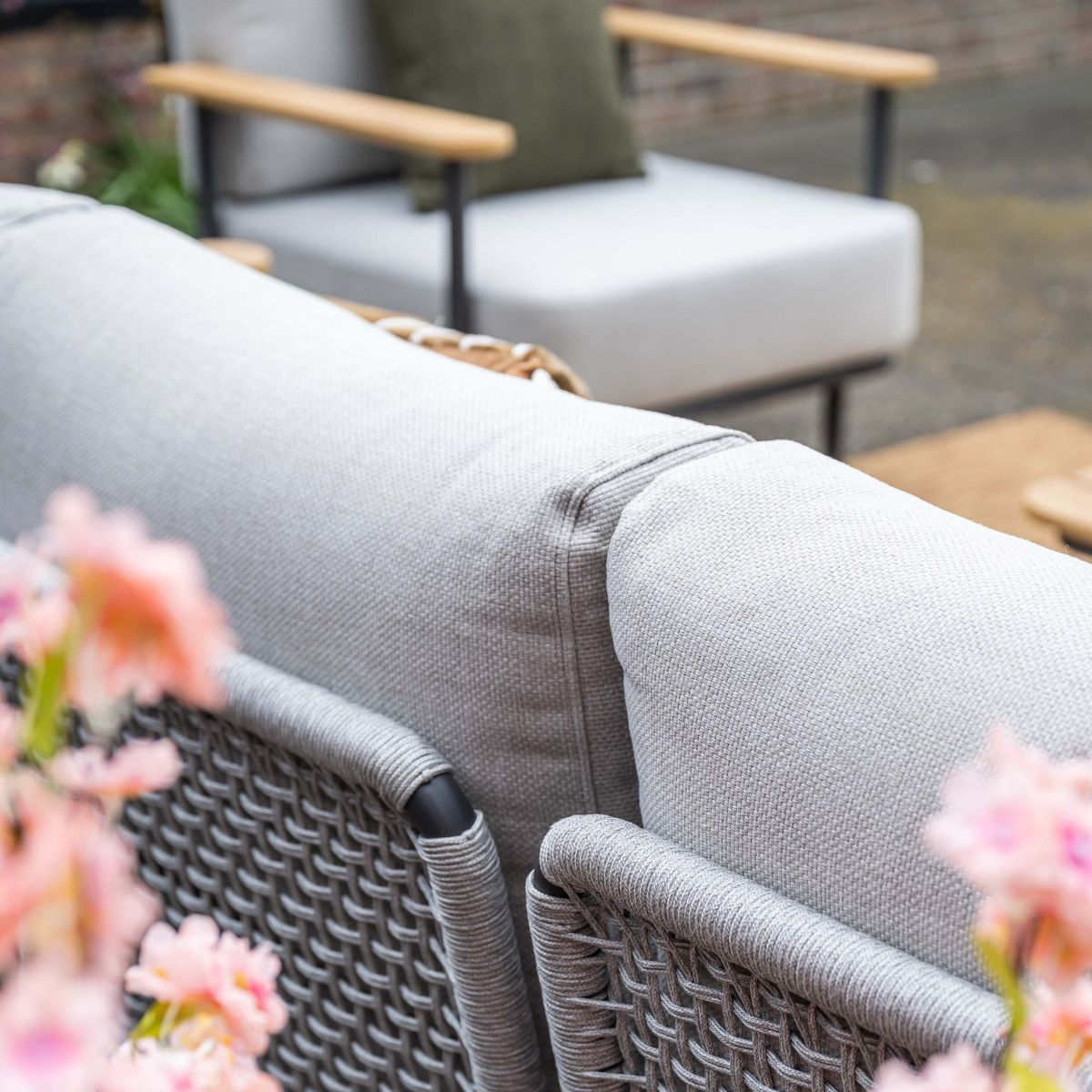 Grey outdoor furniture with cushions and pink flowers in the foreground.