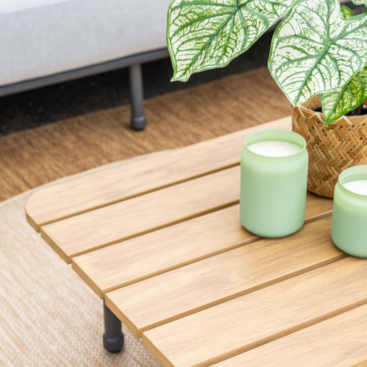 Two green candles sit on a wooden table next to a potted plant.