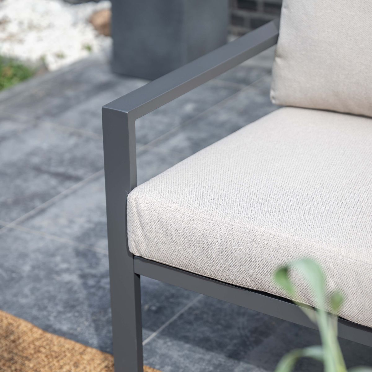 Gray metal chair with light beige cushions on a stone patio.