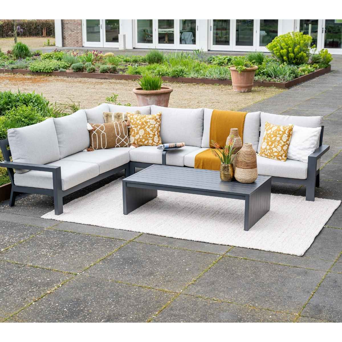 Gray sectional sofa with cushions and coffee table on white rug outdoors.