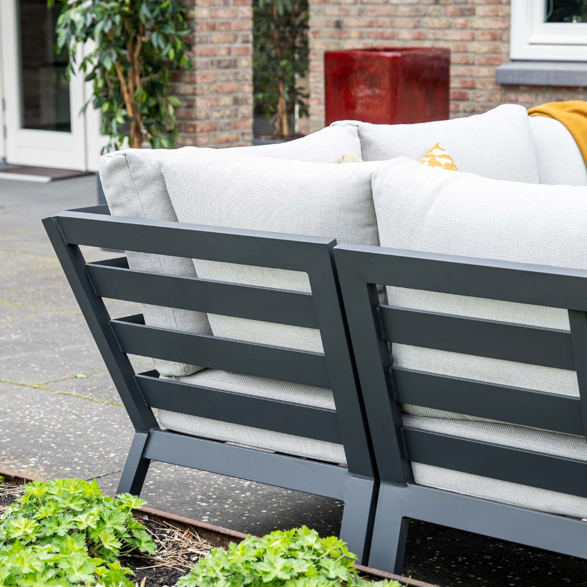 Gray outdoor sofa with light gray cushions and green plants.