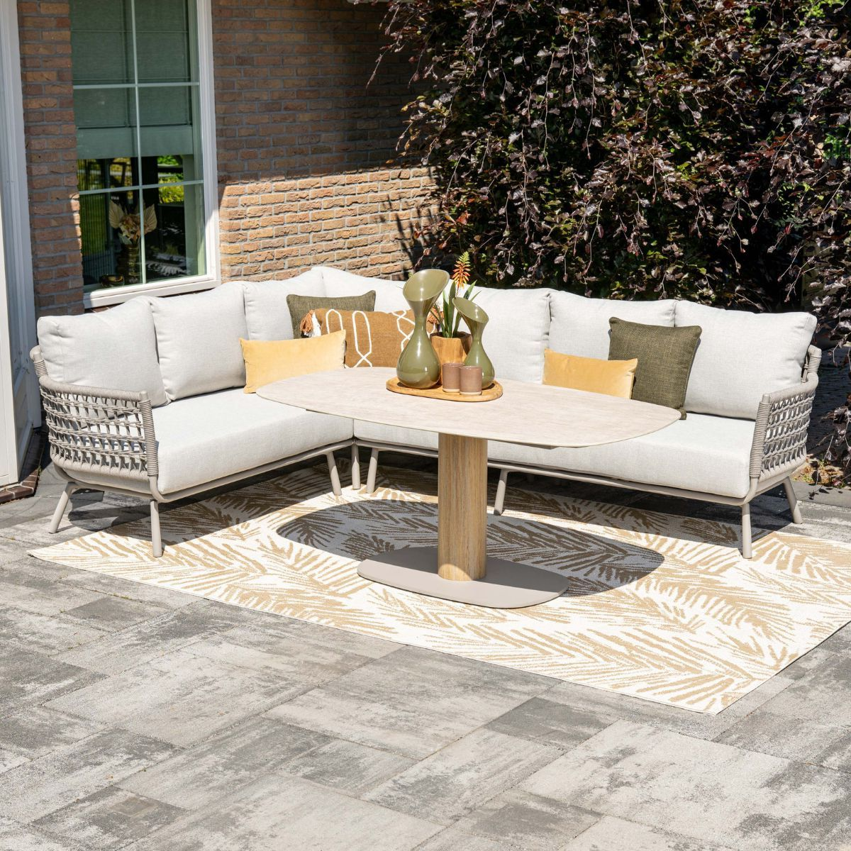 An L-shaped outdoor sofa and table on a patio with a rug.