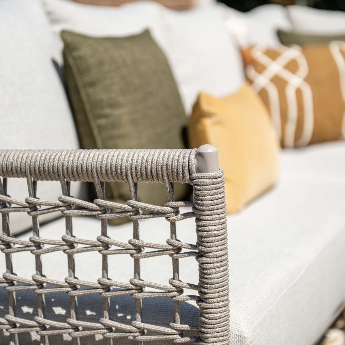 Part of a sofa with rope weave and cushions in green, yellow, and patterned.