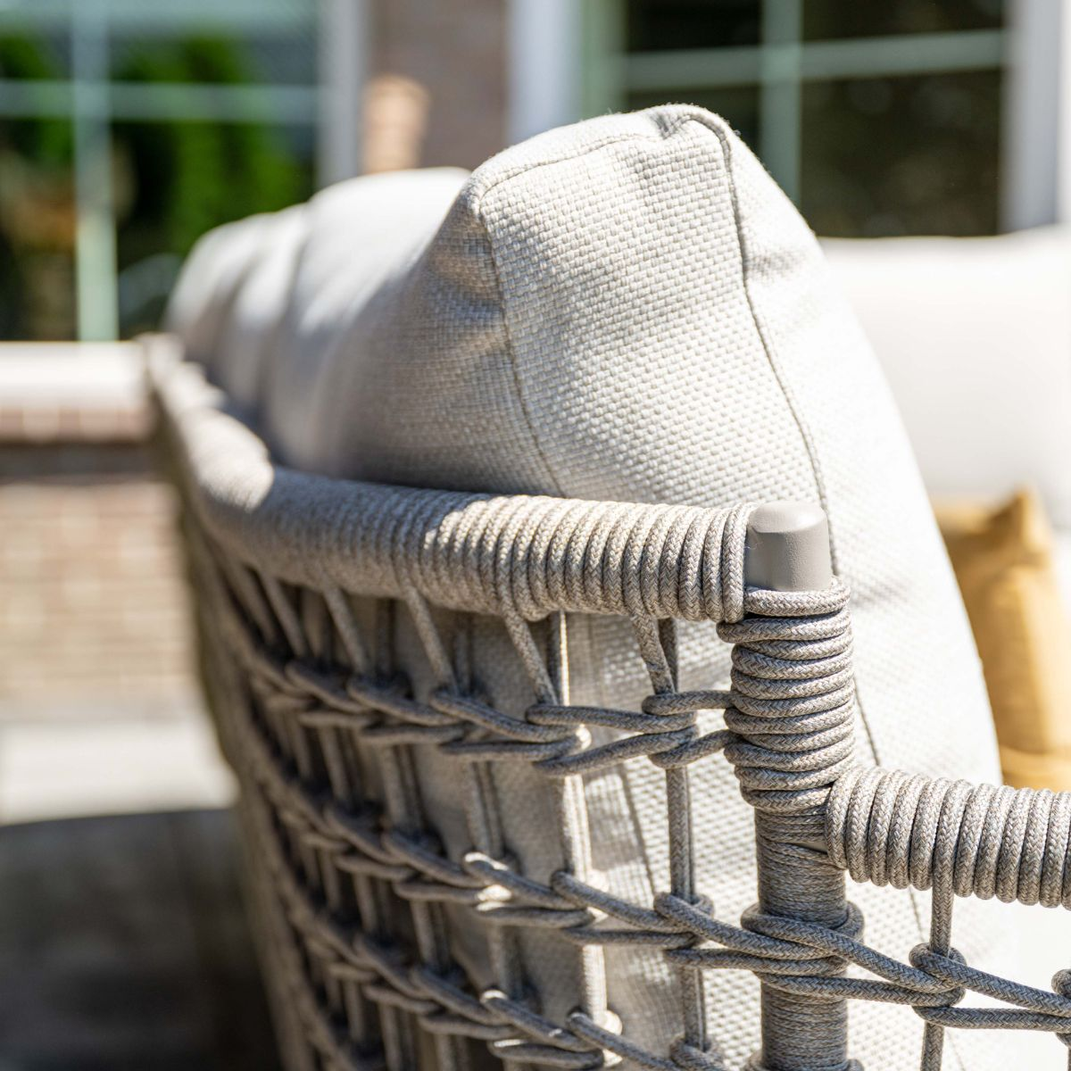 Outdoor grey rattan armchair with beige cushion, with windows in the background.