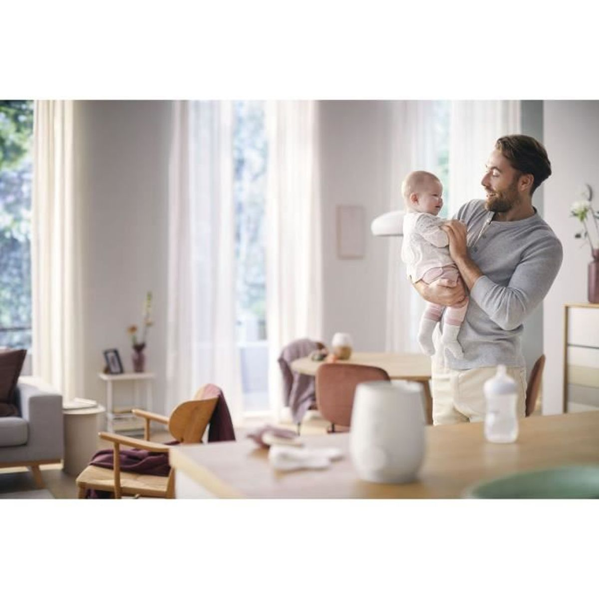 Ein Mann hält ein Baby in einem hellen Wohnzimmer mit Möbeln.