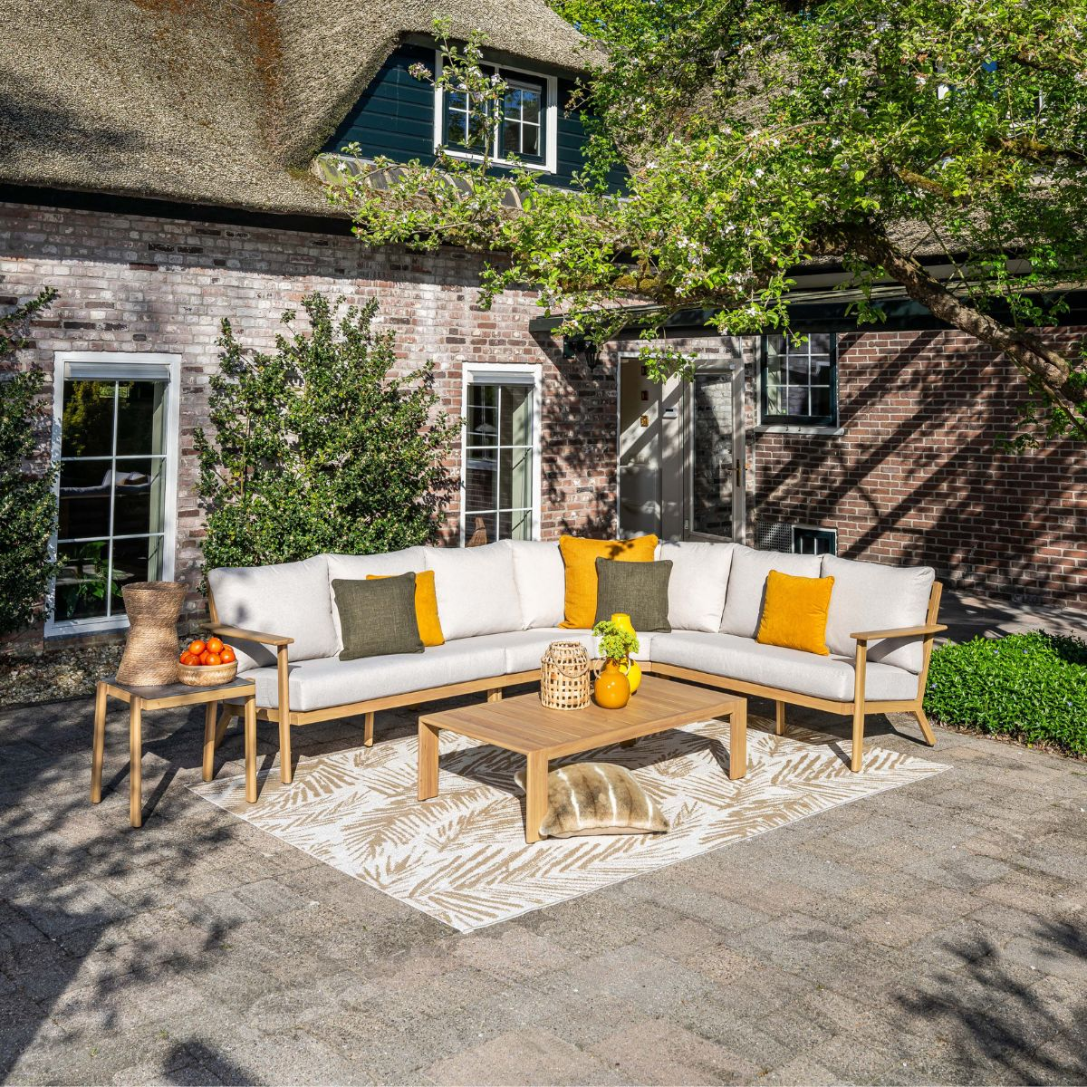 Outdoor sectional sofa with yellow and green pillows on a patio with a thatched roof house.
