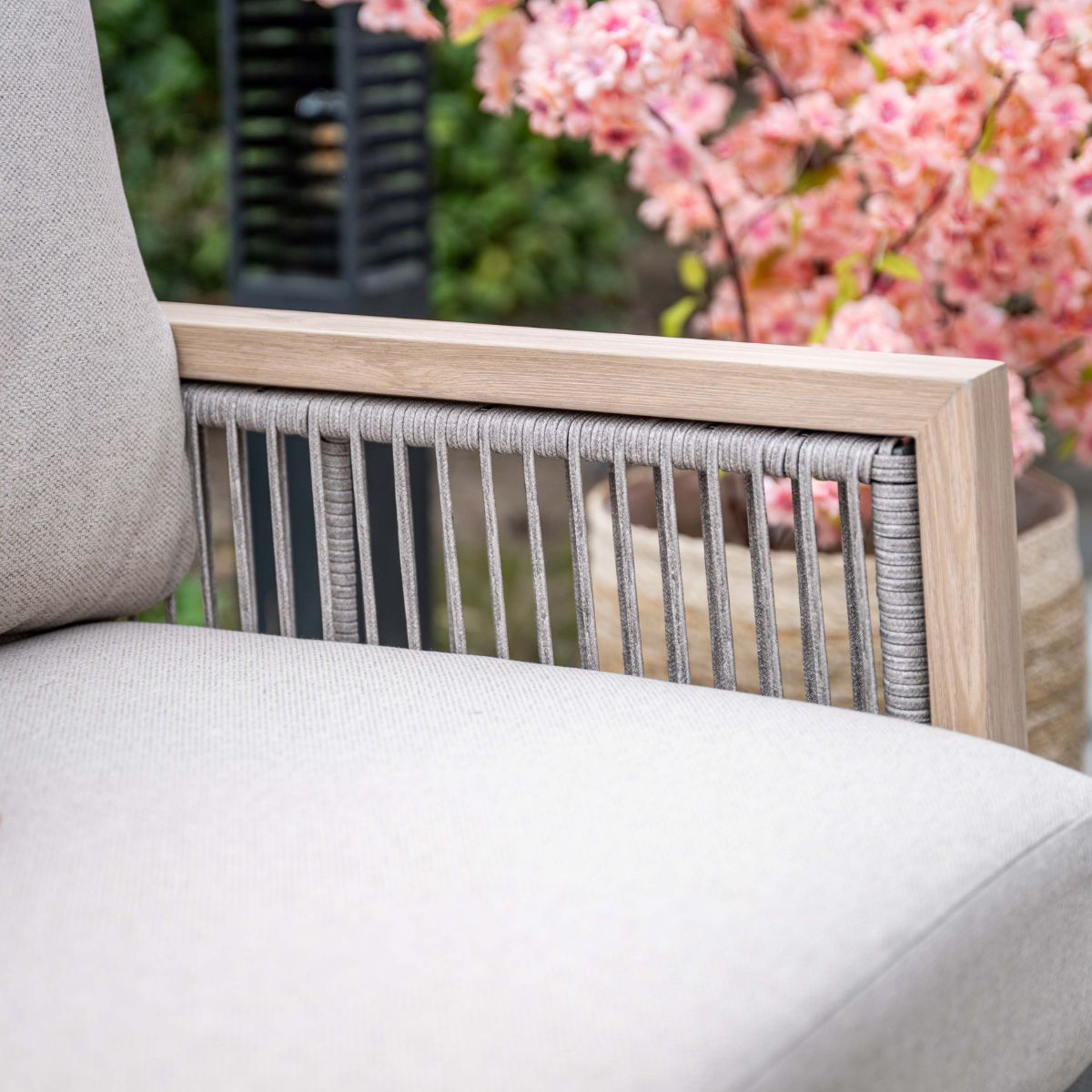 Buitenstoel met houten frame, grijze touwbespanning en lichte kussens.