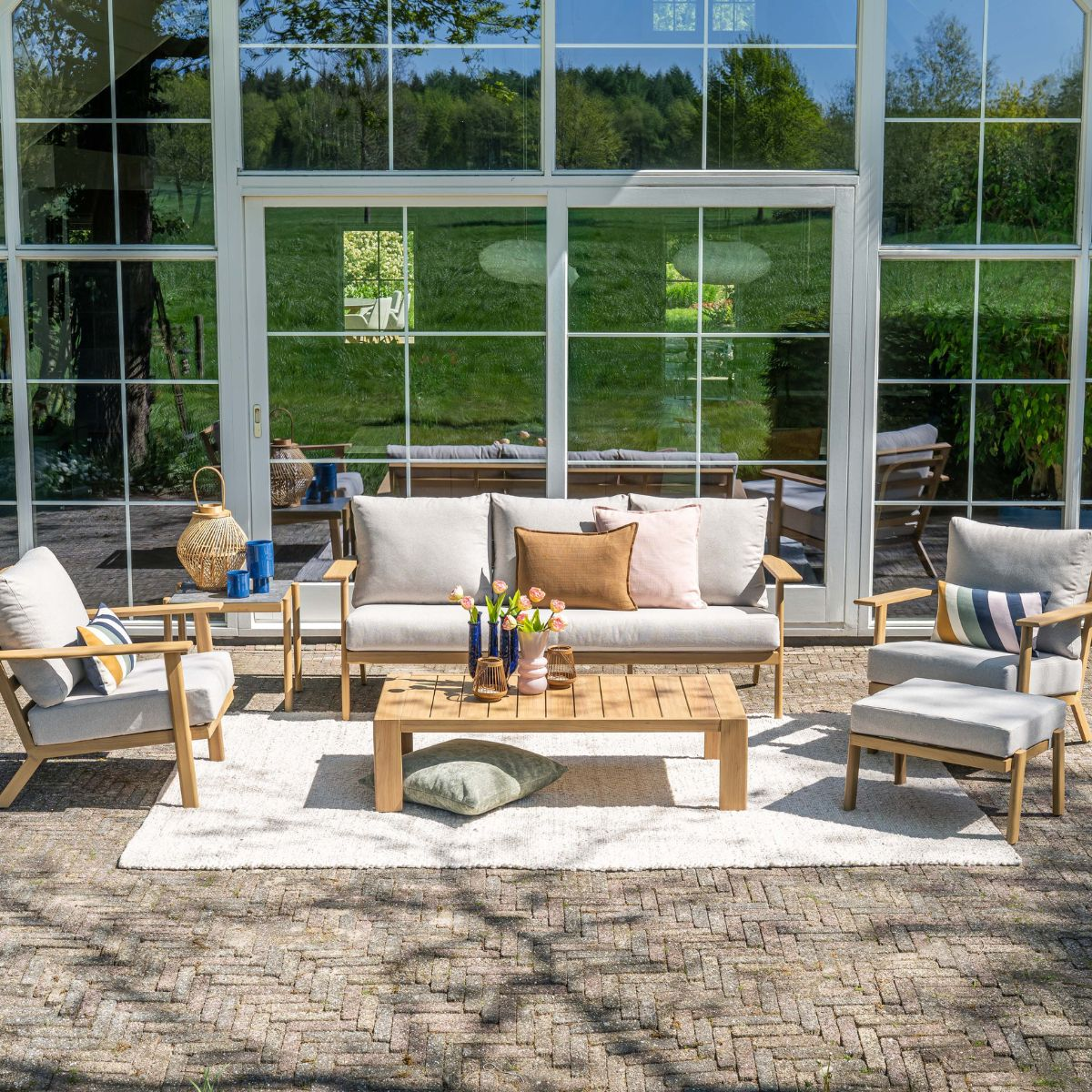 Tuin lounge met bank, fauteuils, salontafel en kleed voor glazen pui.