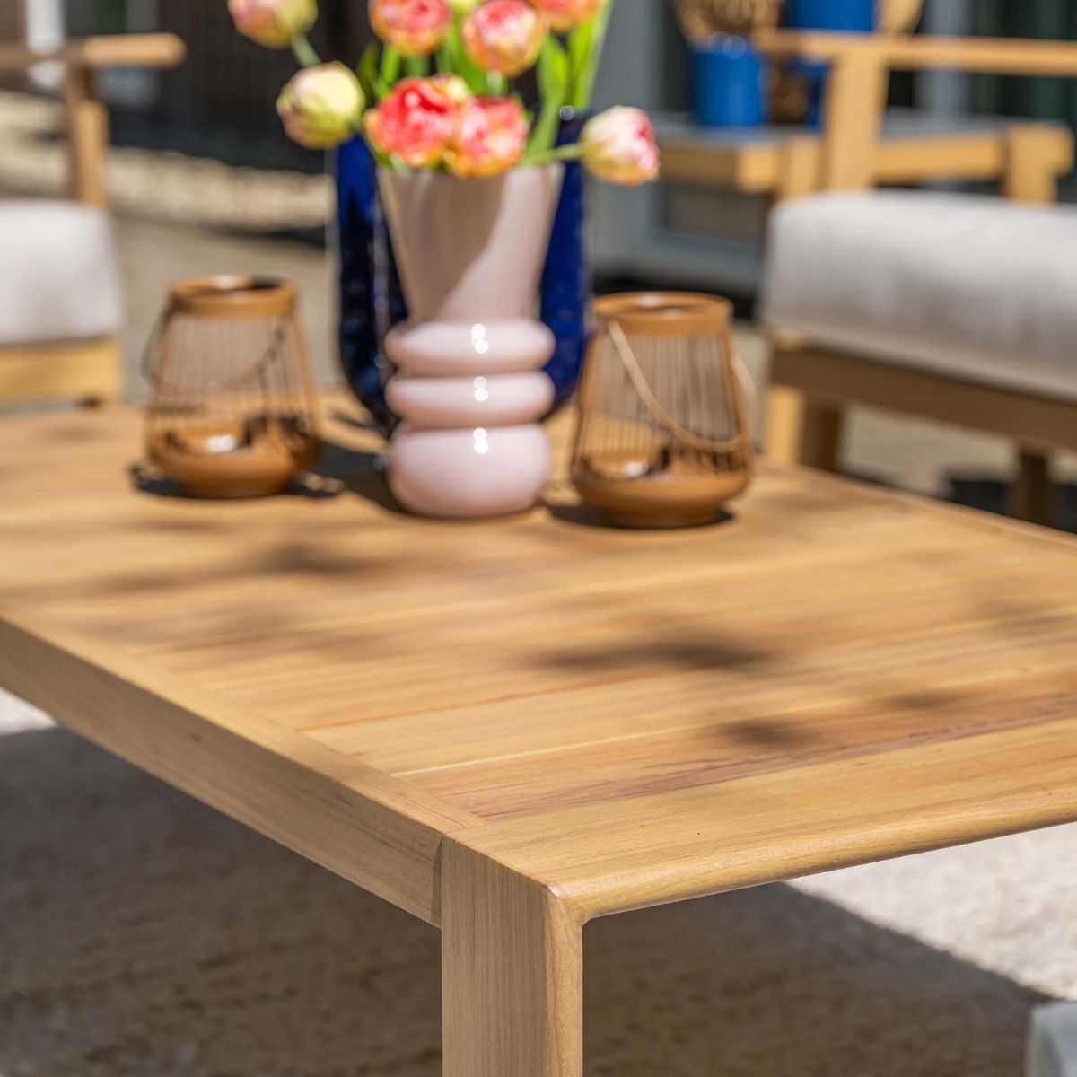 Houten tafel met bloemen in vaas, twee lantaarns en tuinmeubelen achtergrond.