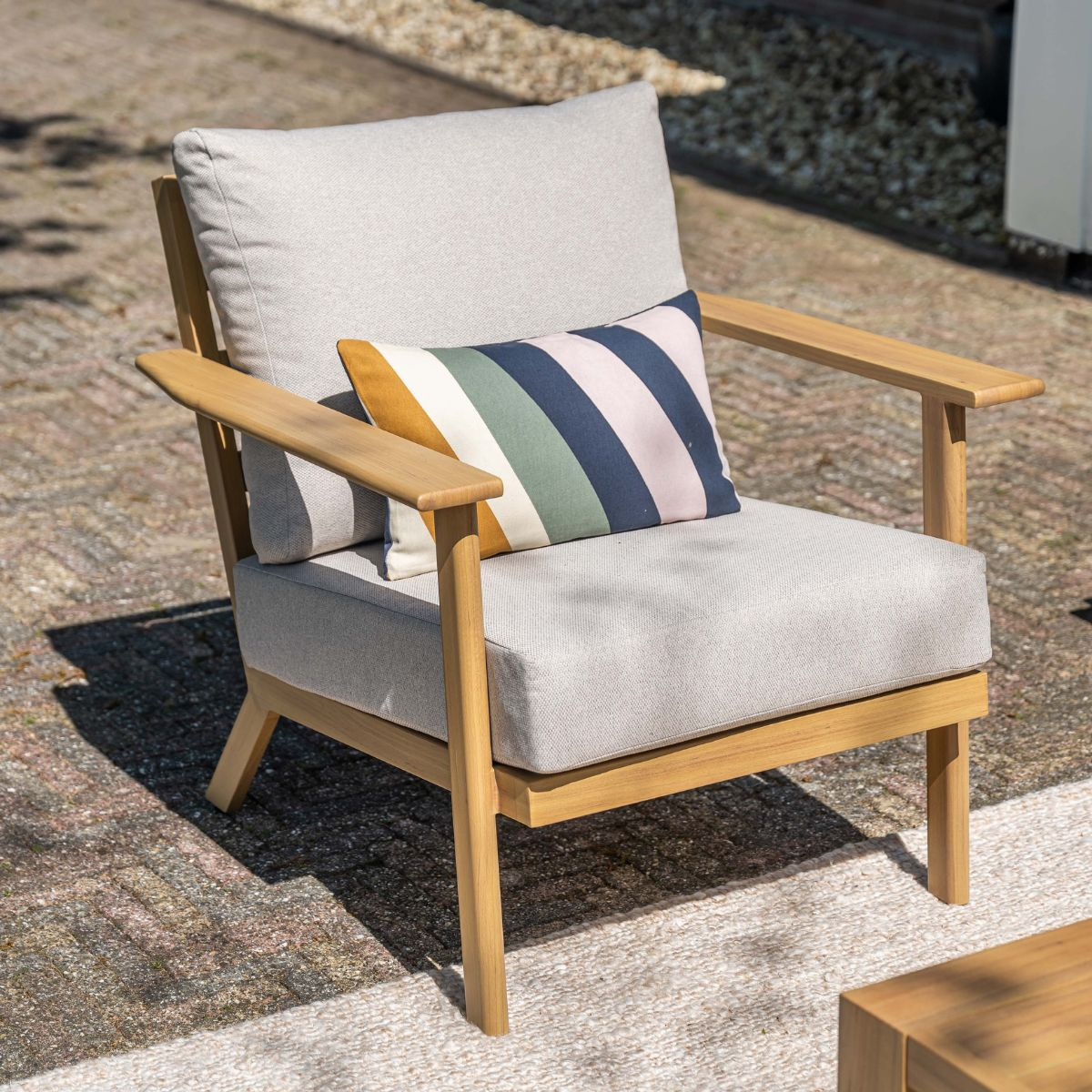 Een grijze fauteuil met houten frame en gestreept kussen op een betegeld terras.