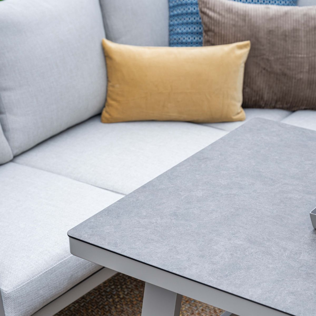 Grijze tafel voor een witte bank met kussens.