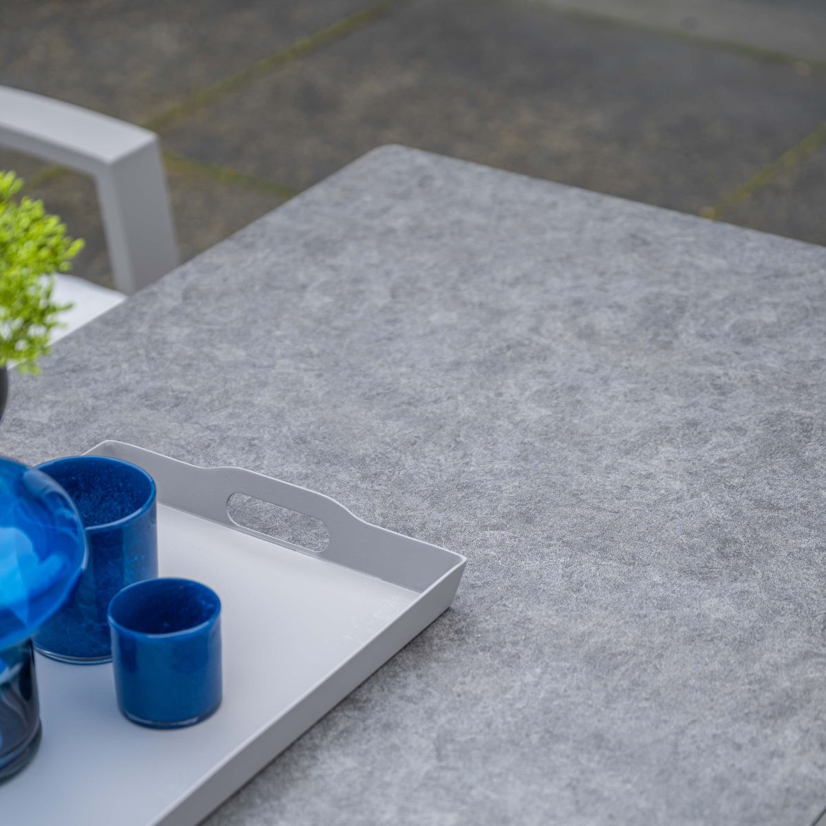 Grijs tafelblad met dienblad, blauwe glazen en groene plant.
