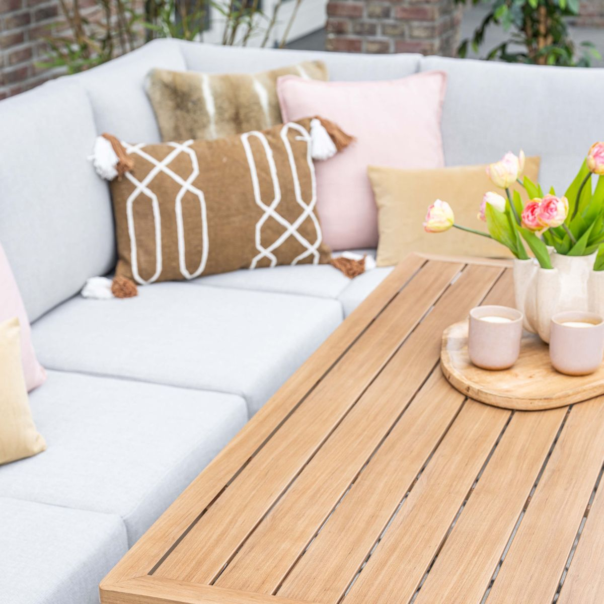 Een buitenhoekbank met decoratieve kussens en tulpen op een houten tafel.