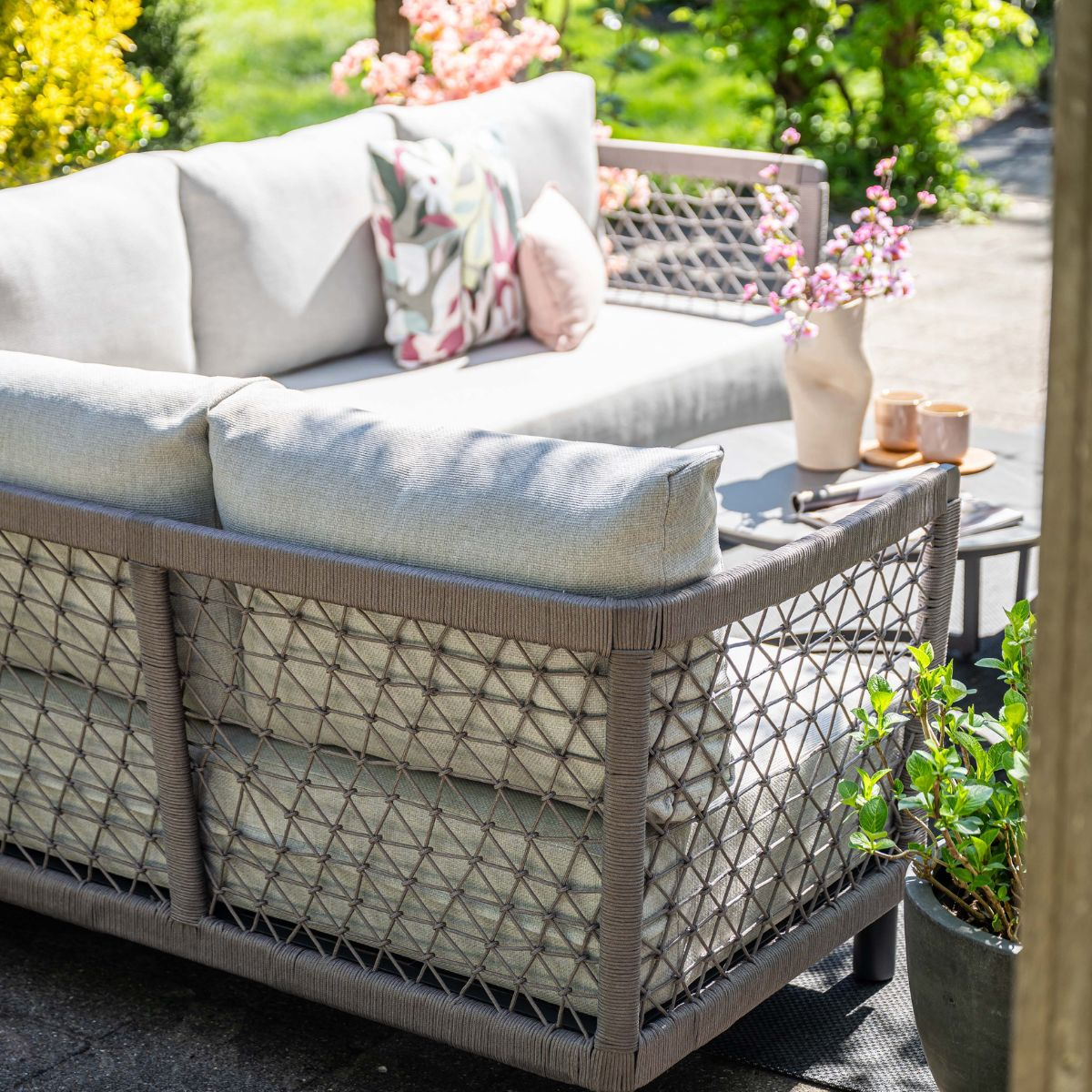Gray outdoor sofa with cushions and flowers in a vase on a table.