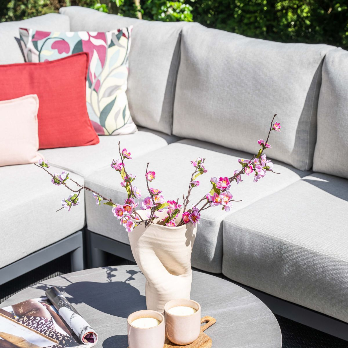 A modern outdoor seating area with a sectional sofa, cushions, and a table with flowers and candles.
