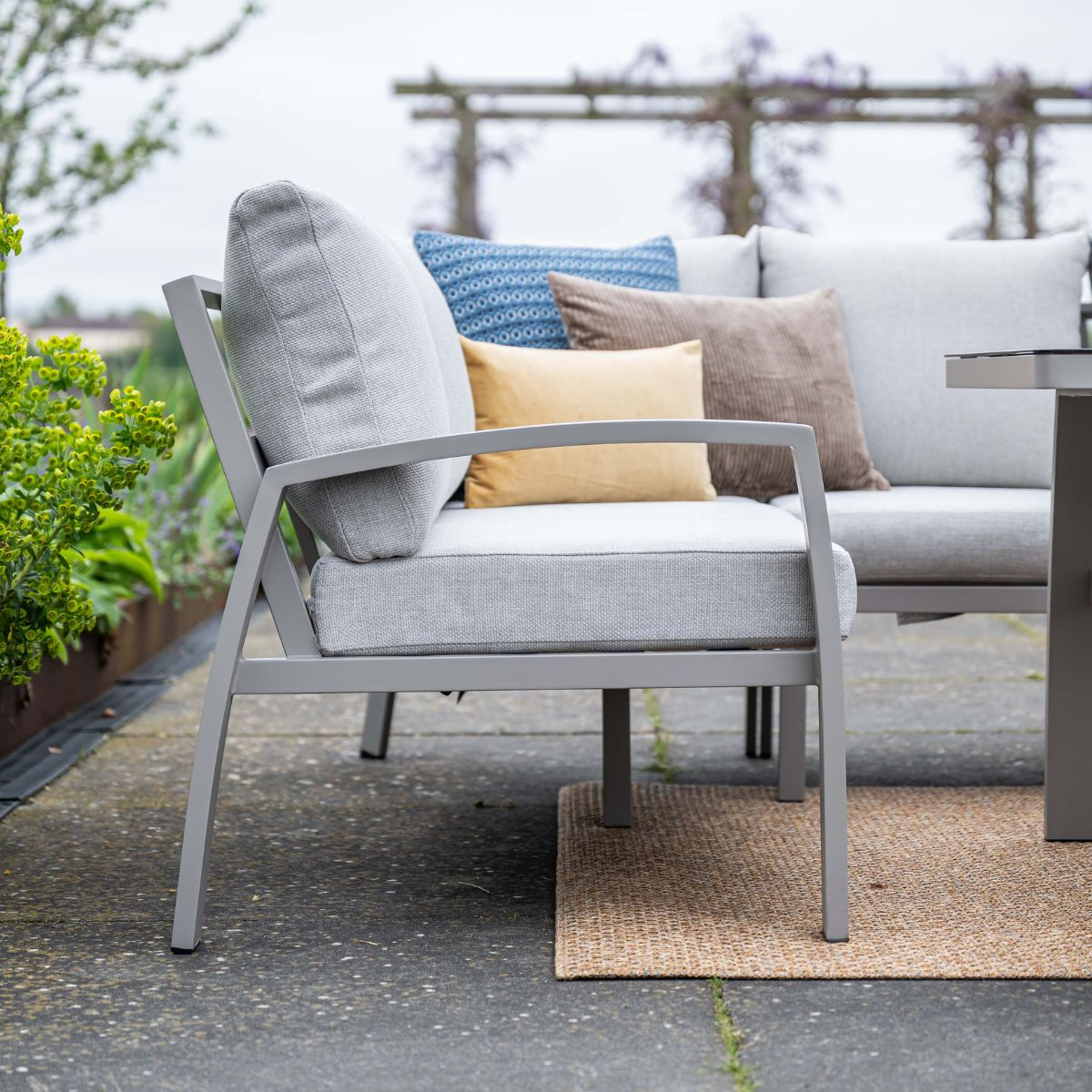 Grijze tuinmeubelen met kussens op een terras met kleed.