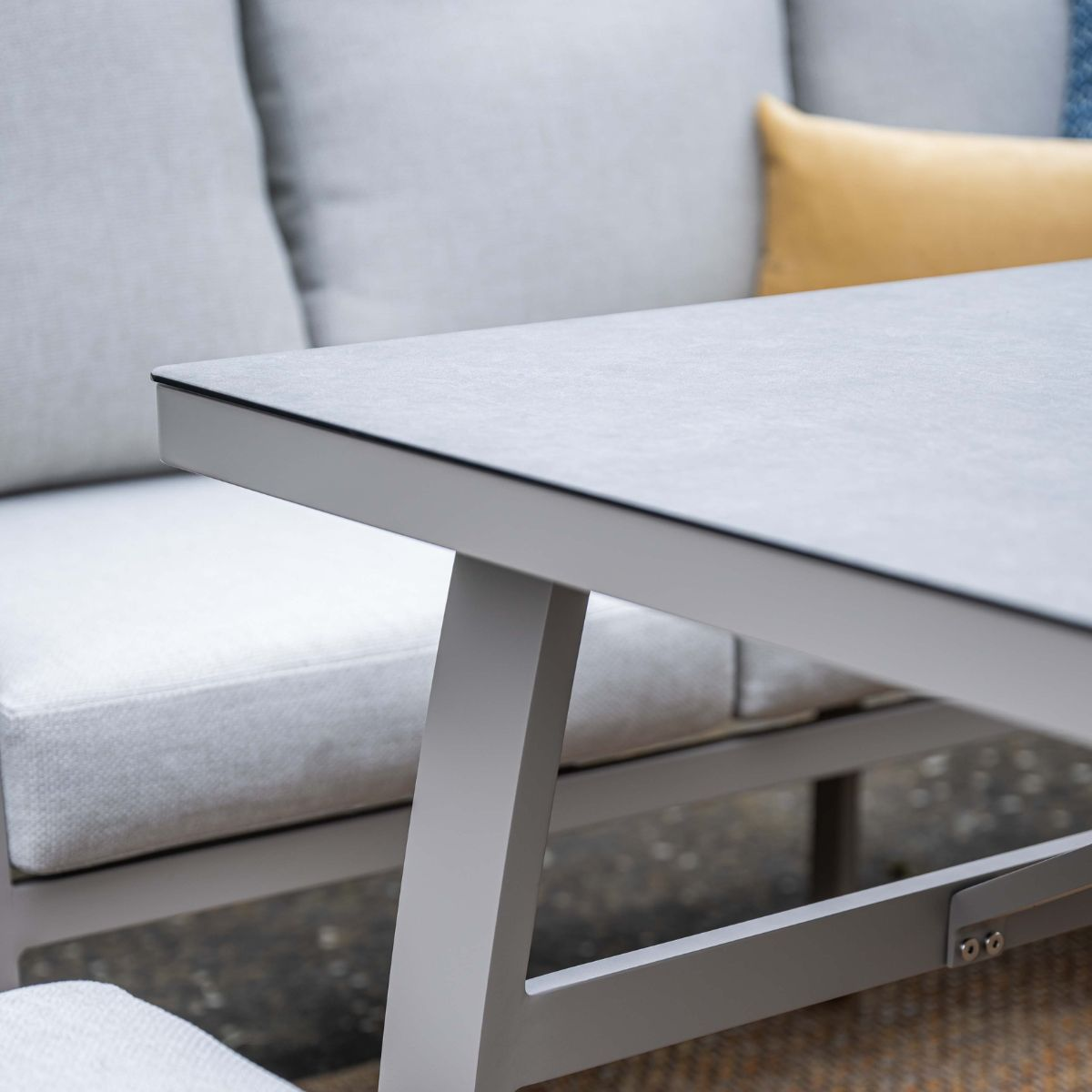 Grijze tafel met beige kussens en een geel kussen op een patio.