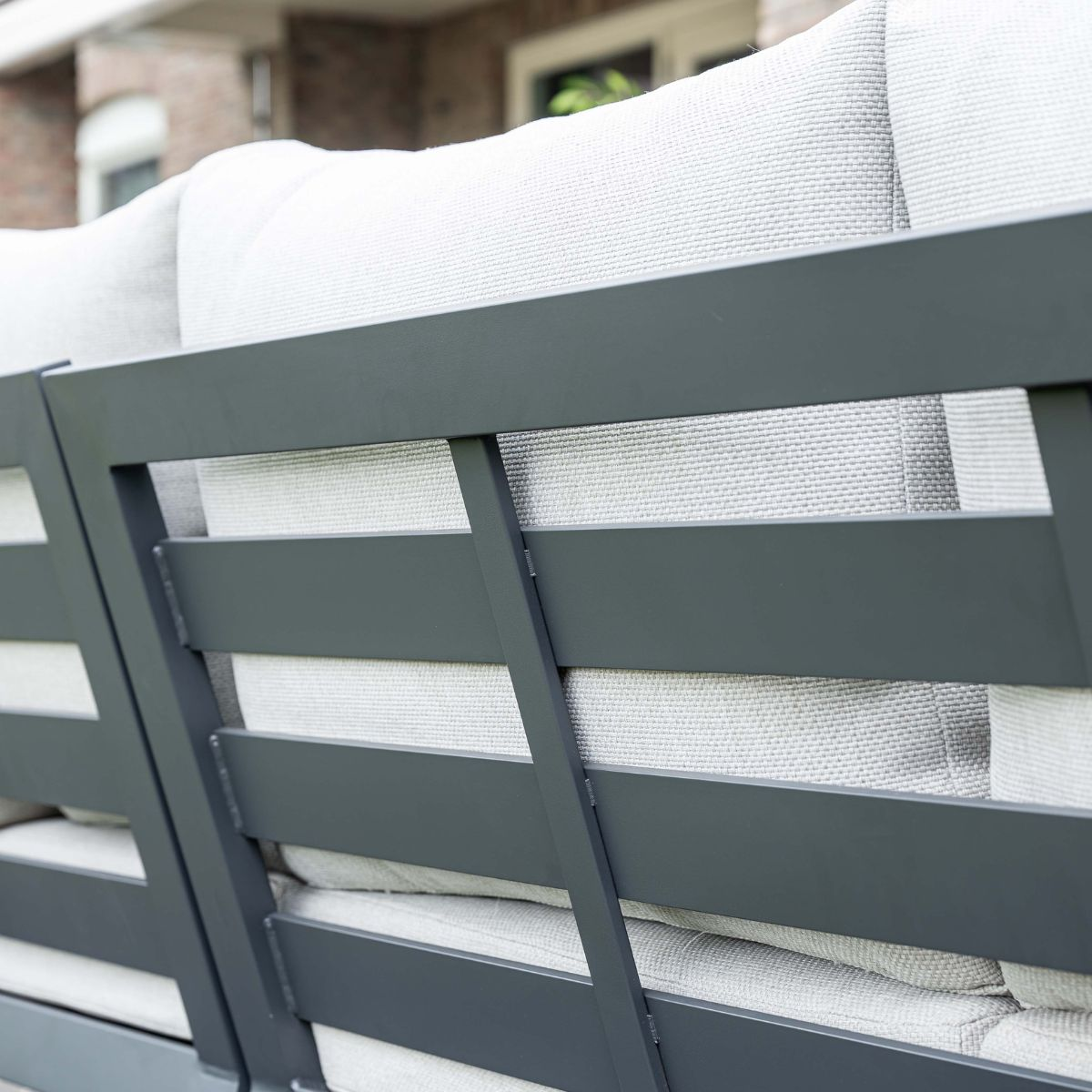 Gray metal frame with light gray cushions, on a patio.