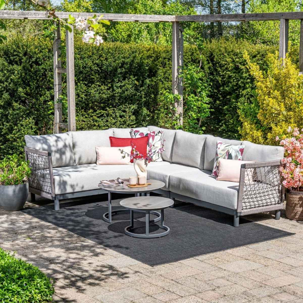A grey sectional sofa with decorative pillows on a patio with two coffee tables.