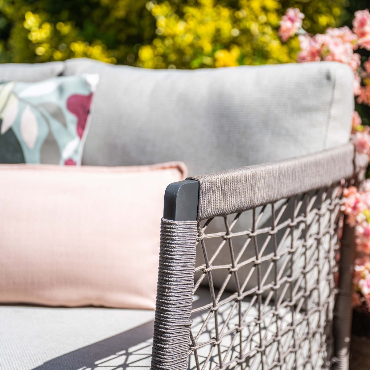 Gray outdoor sofa with cushions and floral background.