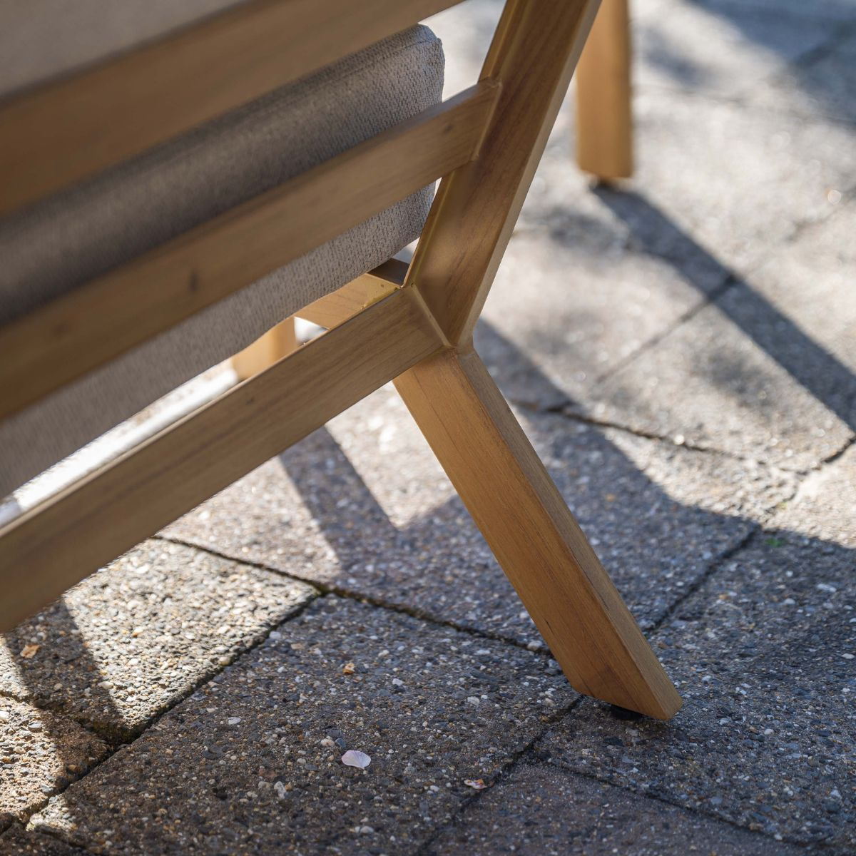 A wooden chair leg stands on a grey stone tile floor in the shade.