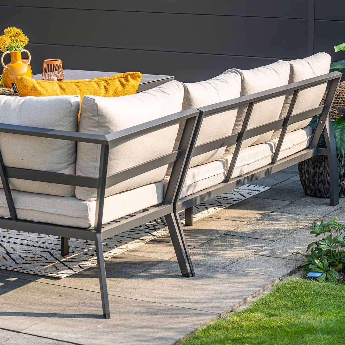 Een moderne buitenbank met beige kussens en metalen frame op een terras.