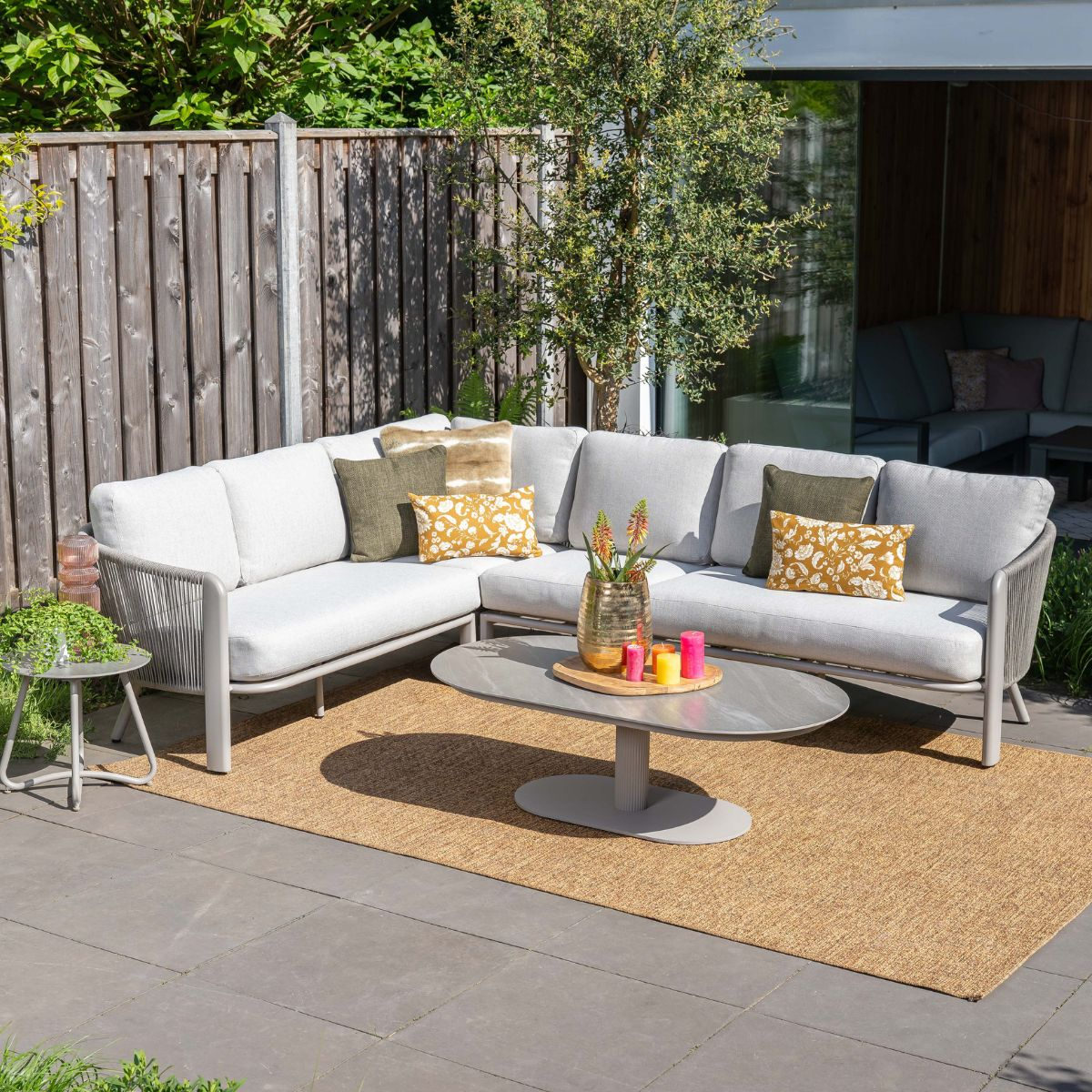 A grey sectional sofa with pillows on a rug on a patio.