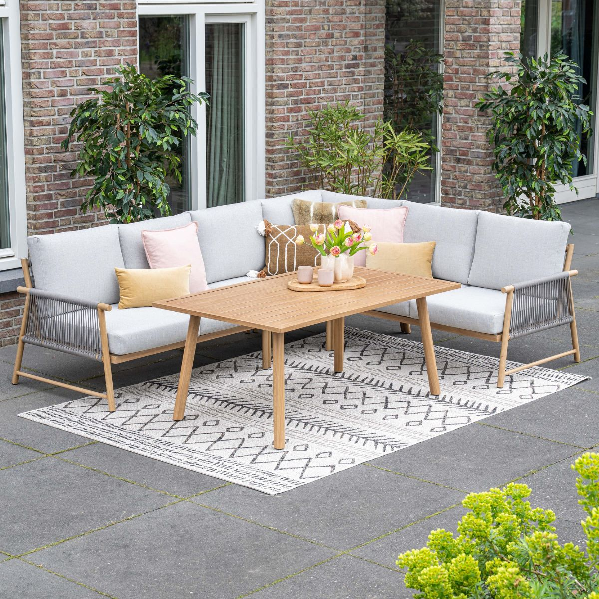 Grijze hoekbank met houten tafel, kleed en kussens op een terras.
