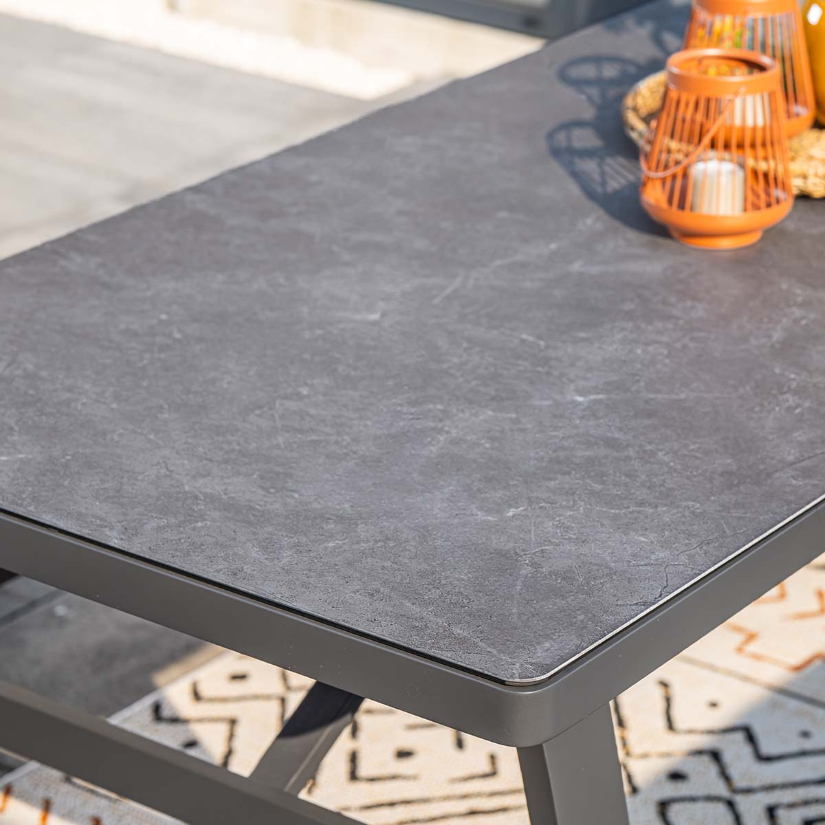 Grijze stenen tafel met oranje lantaarns en een kleed.