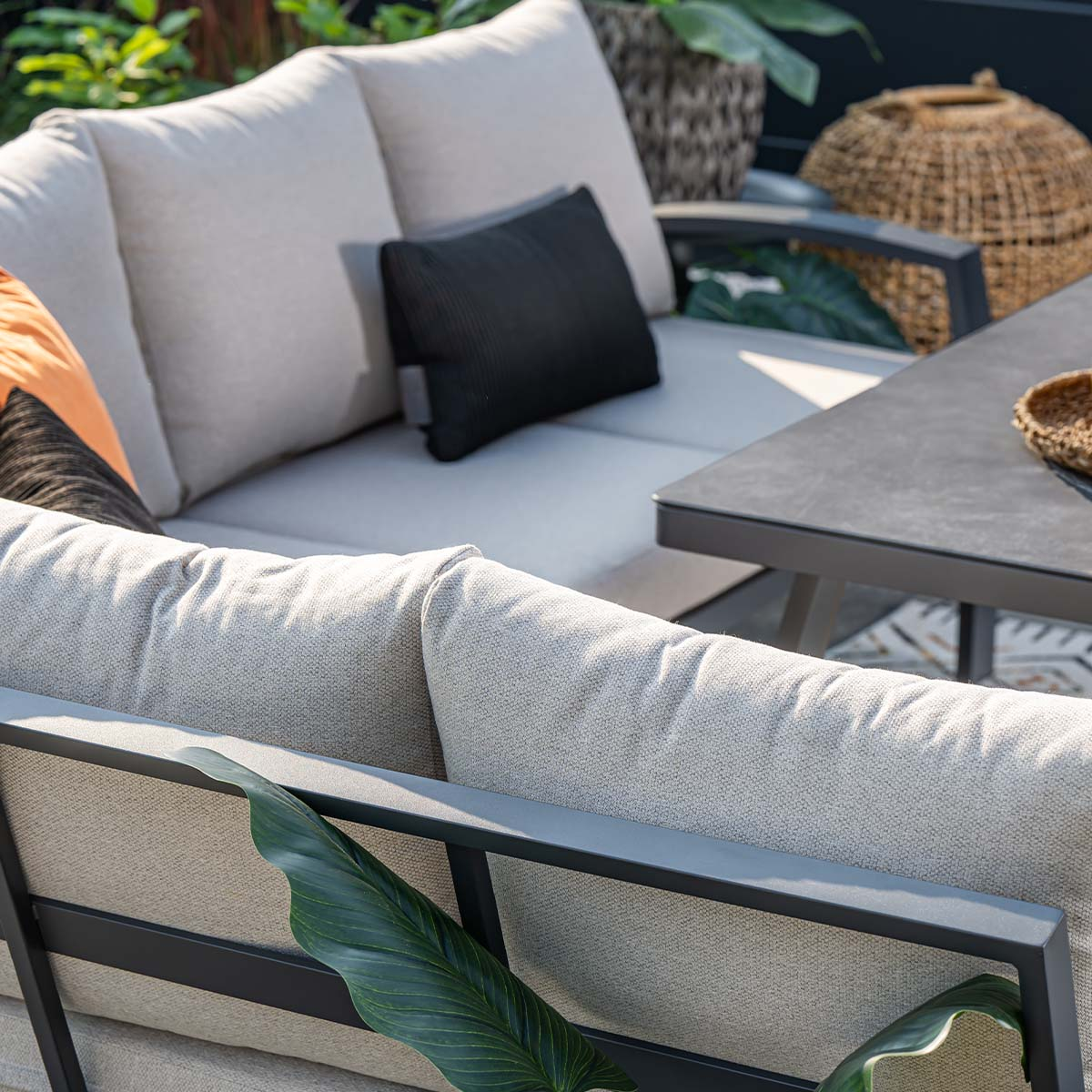 Een beige tuinbank met kussens en een tafel in de tuin.