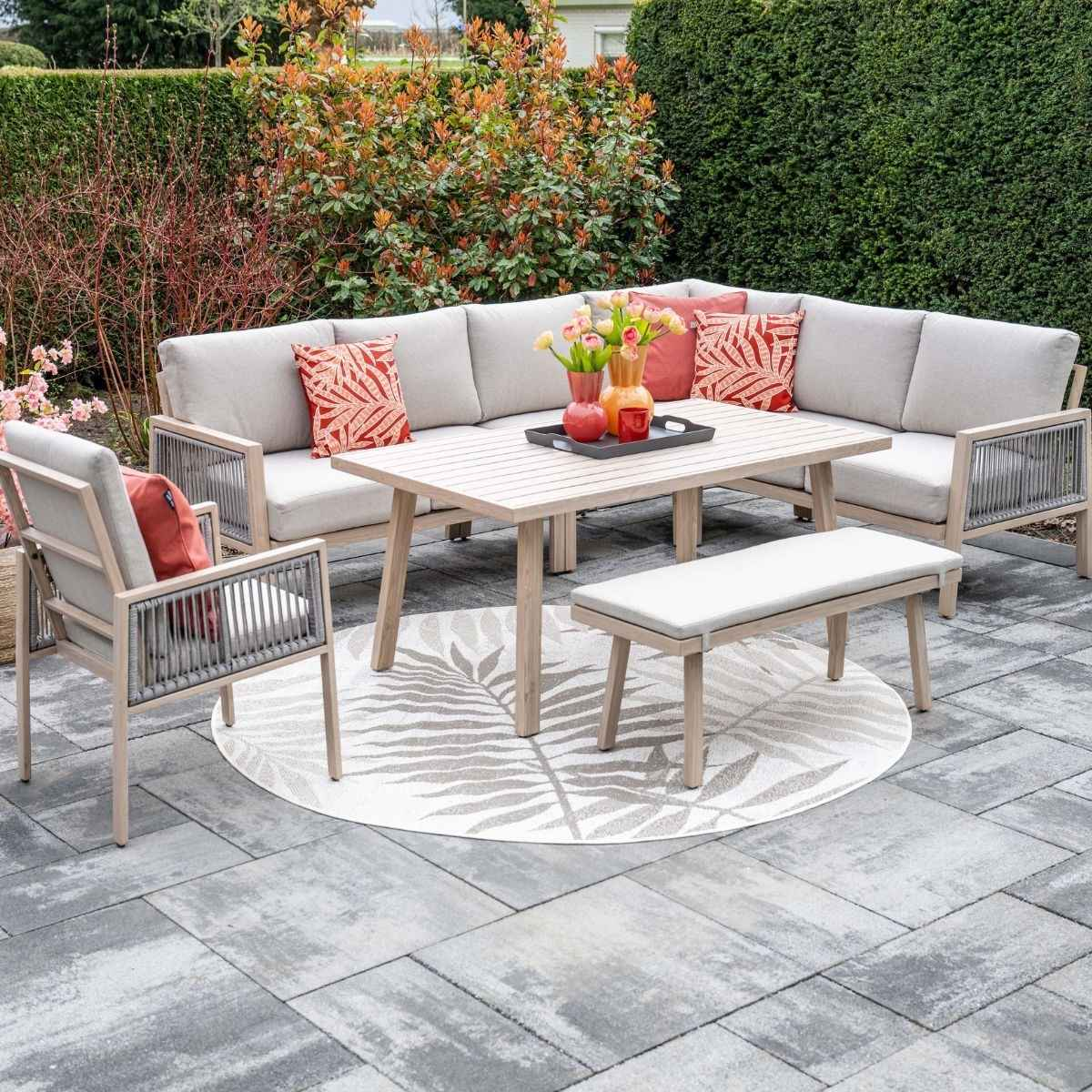 Een hoekbank met tafel, bankje en stoel op een patio met bloemen.