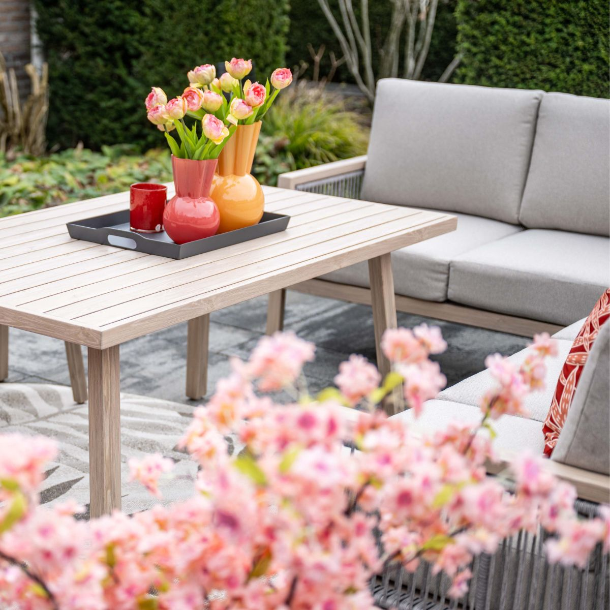 Een houten tafel met vazen en bloemen buiten voor een bank.