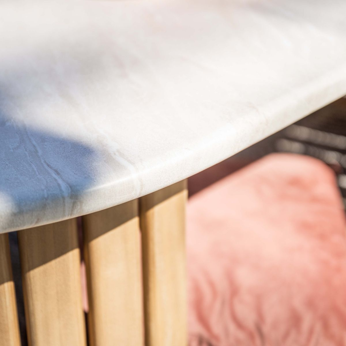 Close-up of a marble-patterned tabletop with wooden accents. A pillow is in the background.