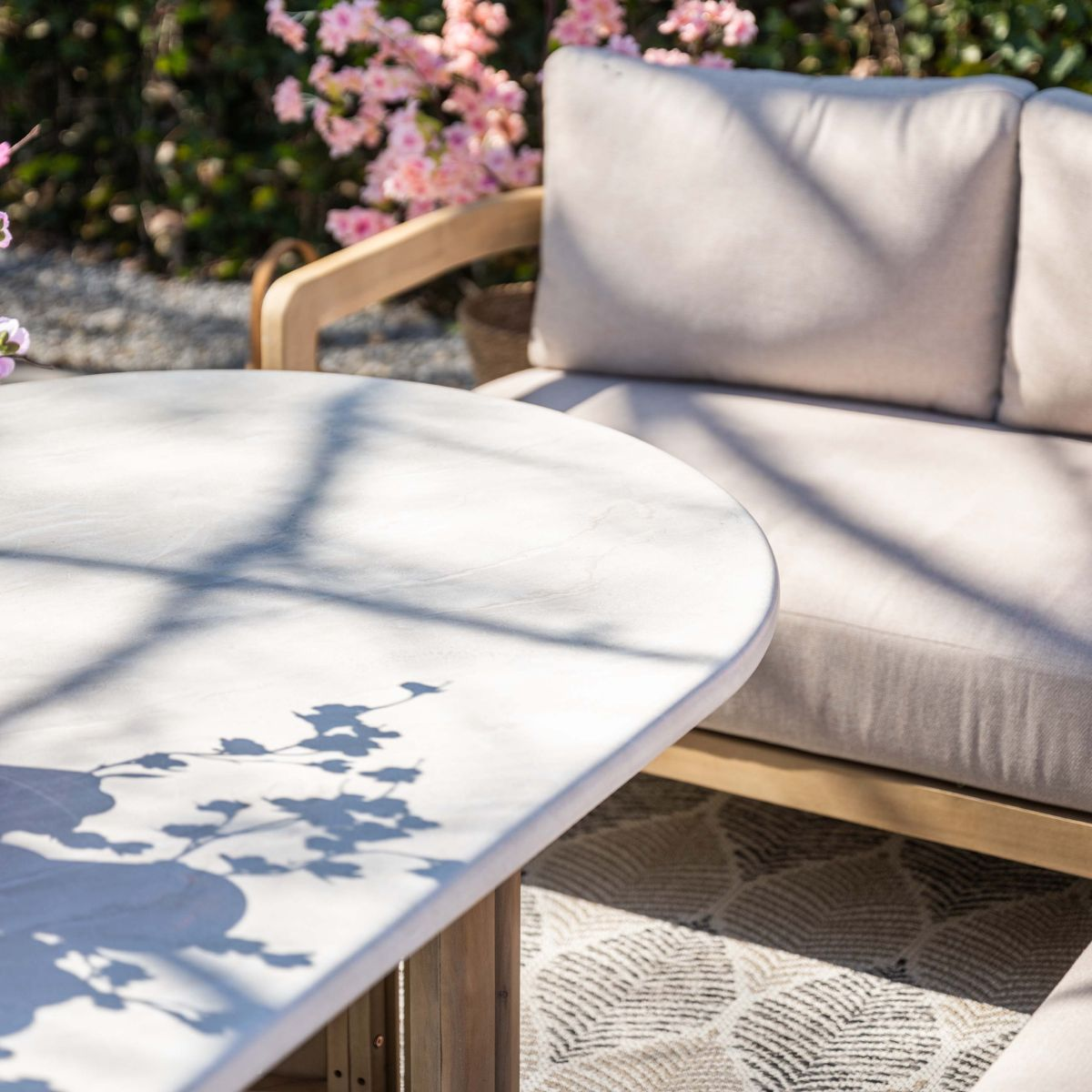Een ronde tafel en een loungeset buiten met roze bloesems op de achtergrond.