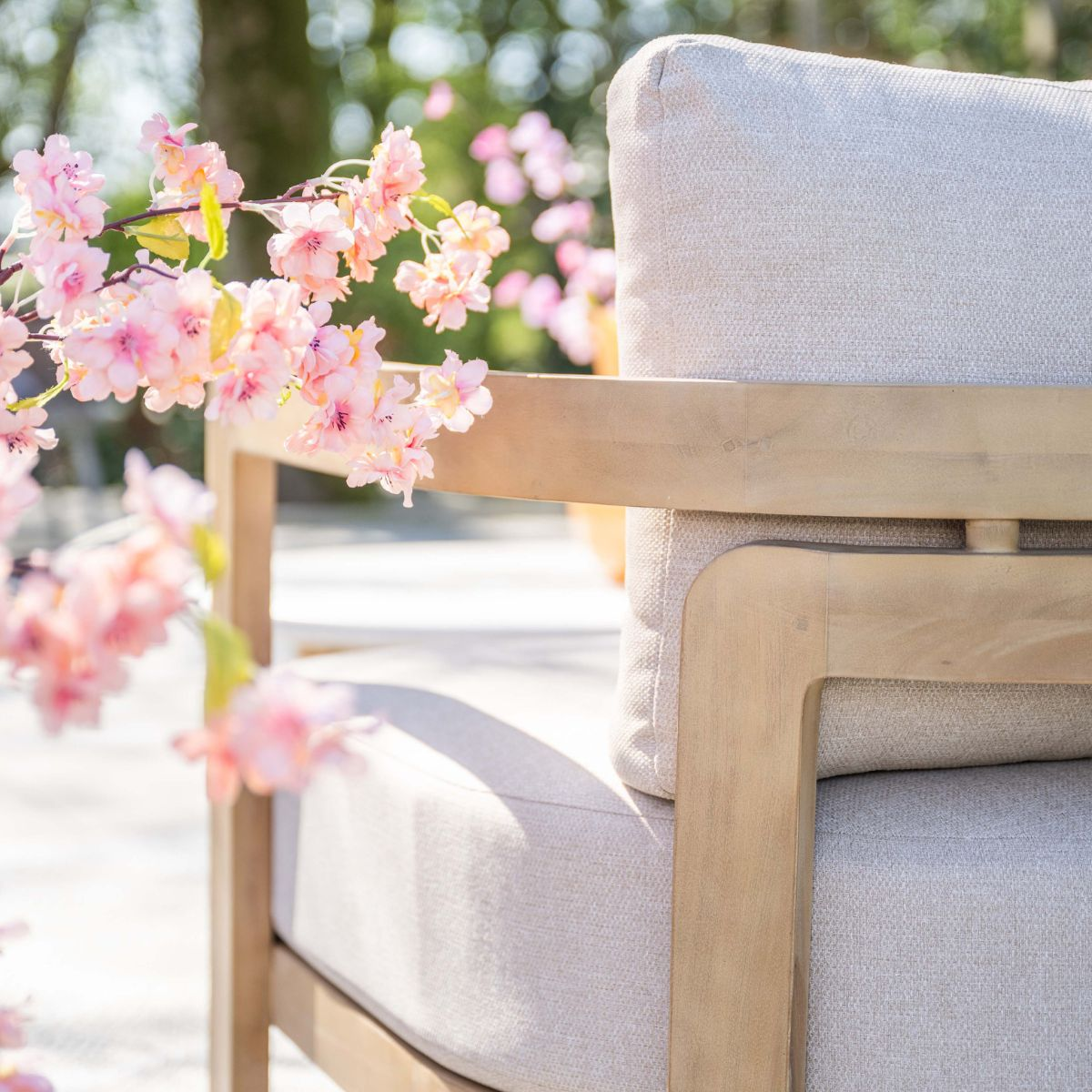 Een lichte fauteuil met kussens, voor bloeiende roze kersenbloesems en bomen.