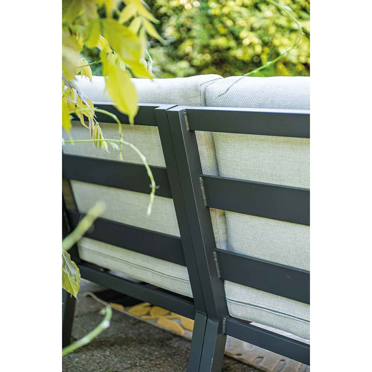Grijze tuinbank met donker metalen frame, omgeven door groen.