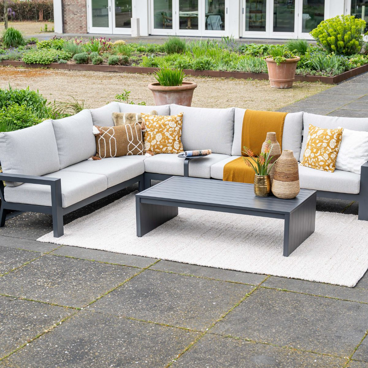 A grey sectional sofa with cushions and a coffee table on an outdoor rug.